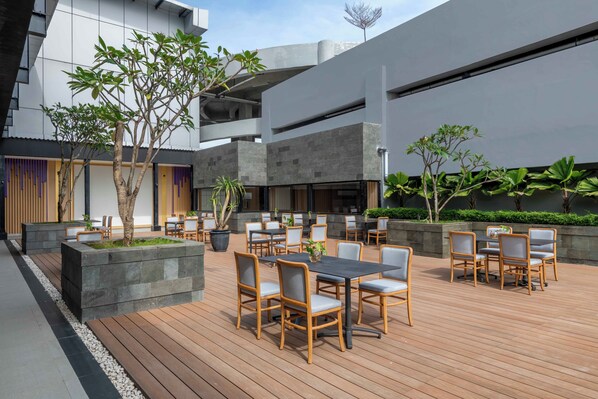 An outdoor patio with wooden flooring, seating arrangements, and potted plants.
