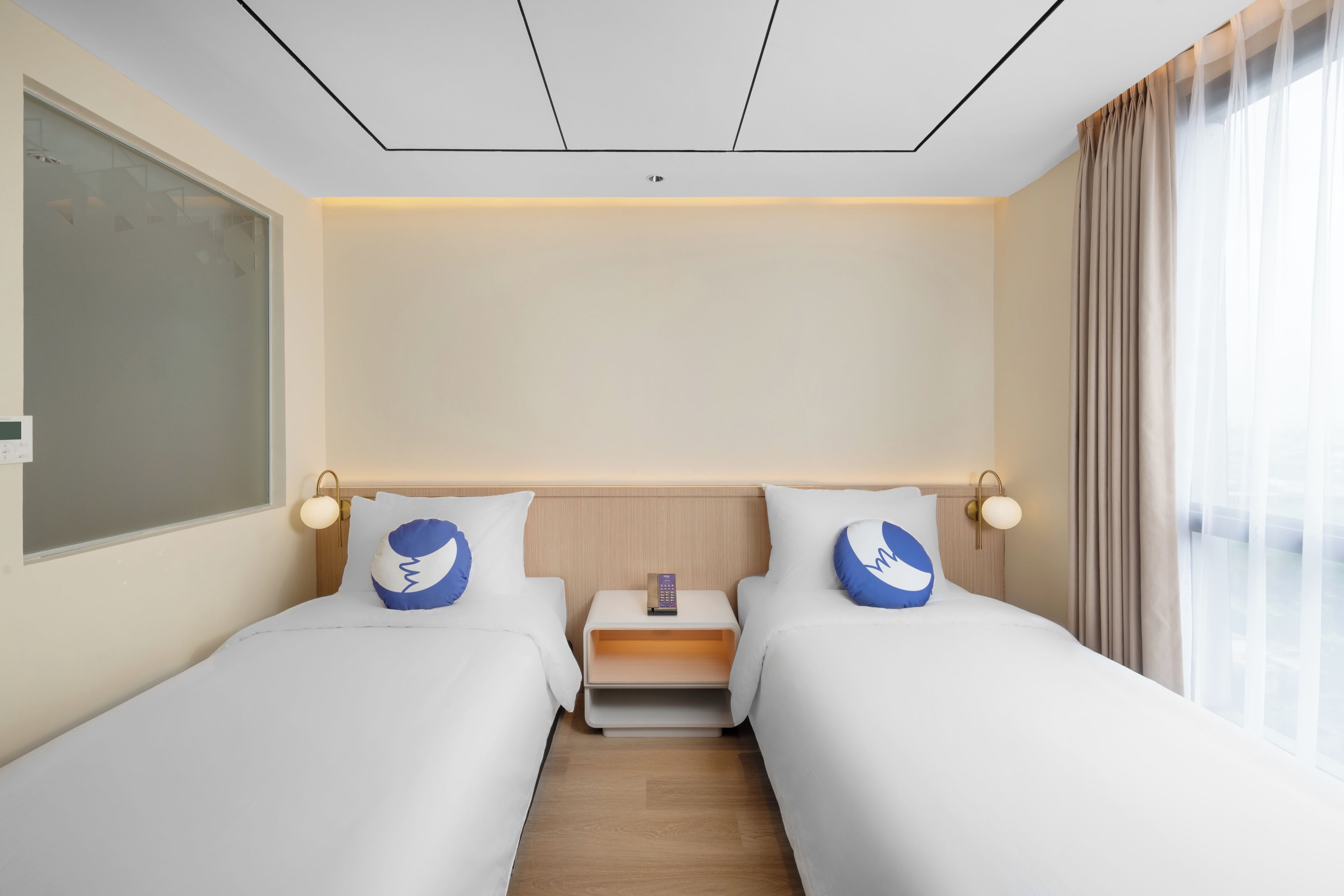 A hotel room with two beds, a nightstand, a wall-mounted phone, and a window with curtains.