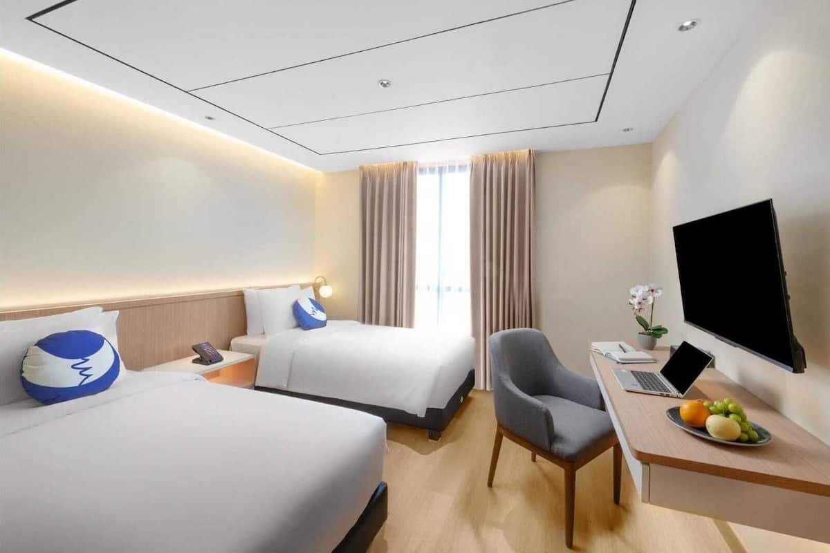Ein Hotelzimmer mit zwei Betten, einem Schreibtisch, einem Laptop, einem Fernseher und einer Obstplatte.