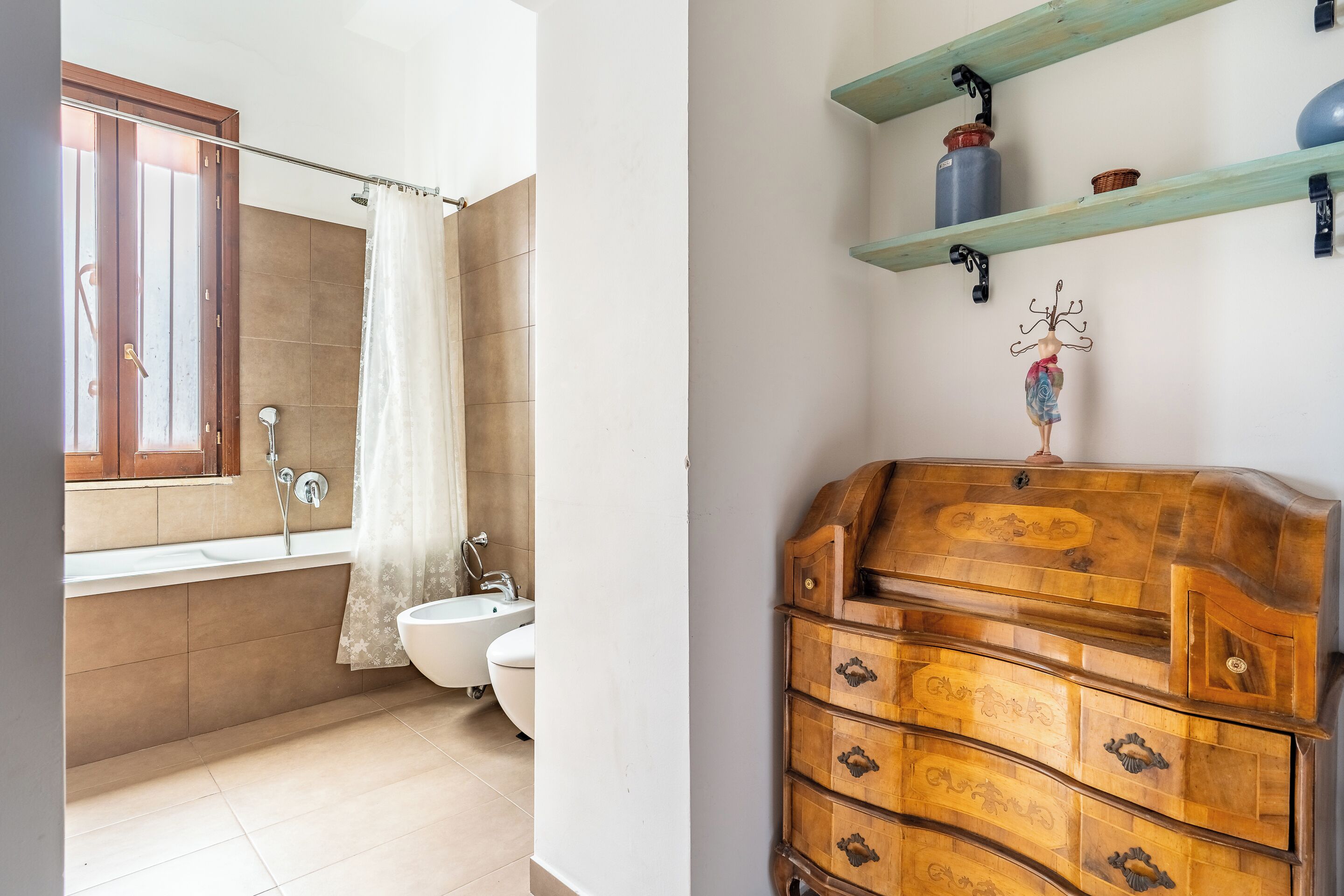 A bathroom with a bathtub, toilet, and sink. There is a wooden dresser with drawers and a decorative item on top.