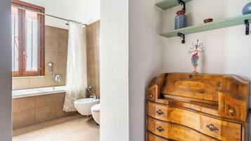 A bathroom with a bathtub, toilet, and sink. There is a wooden dresser with drawers and a decorative item on top.