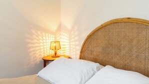 A neatly made bed with white linens, a wicker headboard, and a small bedside table with a lamp casting a warm glow. - Siracusa Horizon Home by Wonderful Italy (Syracuse)
