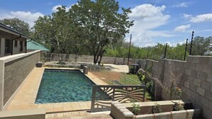 Une piscine dotée d’une plage en pierre, entourée d’un petit muret de pierre et d’un portail en métal.