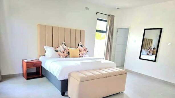 Une chambre moderne avec un grand lit, une table de chevet, un banc, une fenêtre avec des rideaux et un miroir sur le mur.