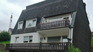 A two-story house with a balcony, a garage, and potted plants.