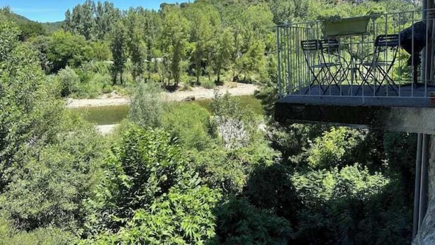 A balcony with a chair and table overlooking a river and forested area. - The Bamboo Lodge with its feet in the water (Anduze)