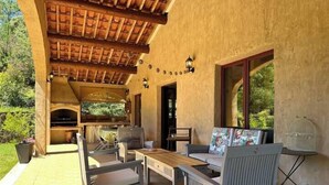 An outdoor patio with a wooden table and chairs, a barbecue grill, and a birdcage. - Beautiful Cevennes farmhouse with swimming pool (Corbès)