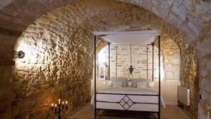 Una habitación con paredes de piedra, una cama con dosel, un candelabro y un arco de piedra.