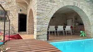 Un espacio al aire libre con paredes de piedra, una piscina, una terraza de madera y asientos.