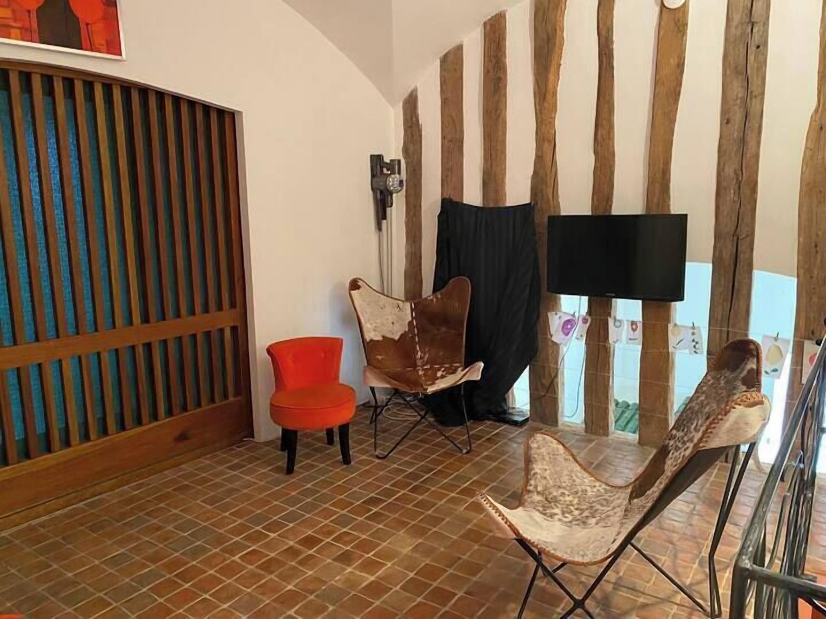 A room with a tiled floor, a wooden slat partition, a red chair, a brown leather chair, and a television mounted on the wall.