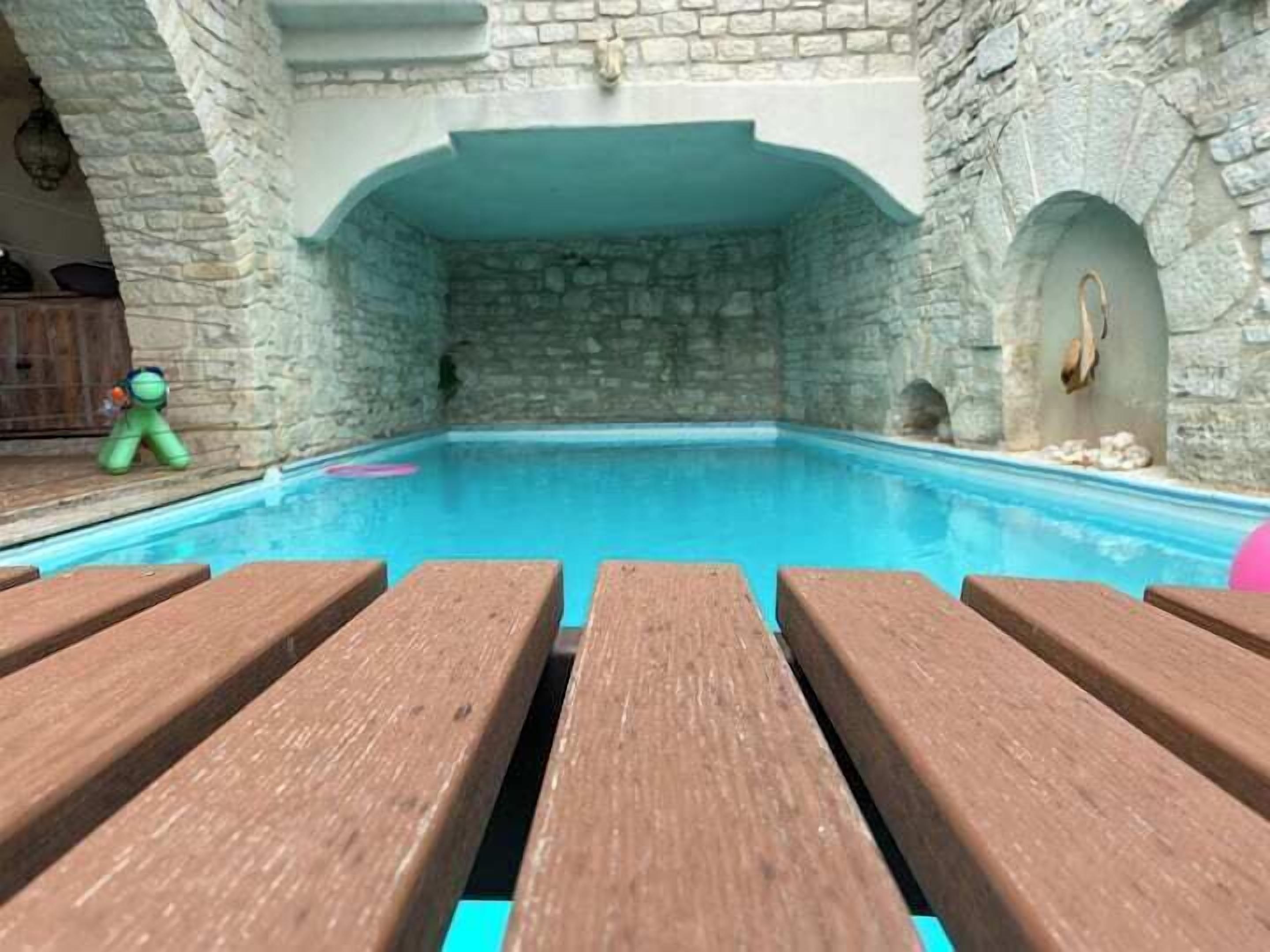 Une piscine intérieure aux murs de pierre, avec des bancs en bois en premier plan.