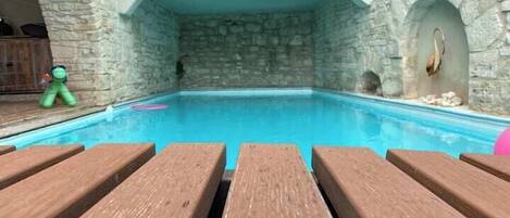 Une piscine intérieure aux murs de pierre, avec des bancs en bois en premier plan.