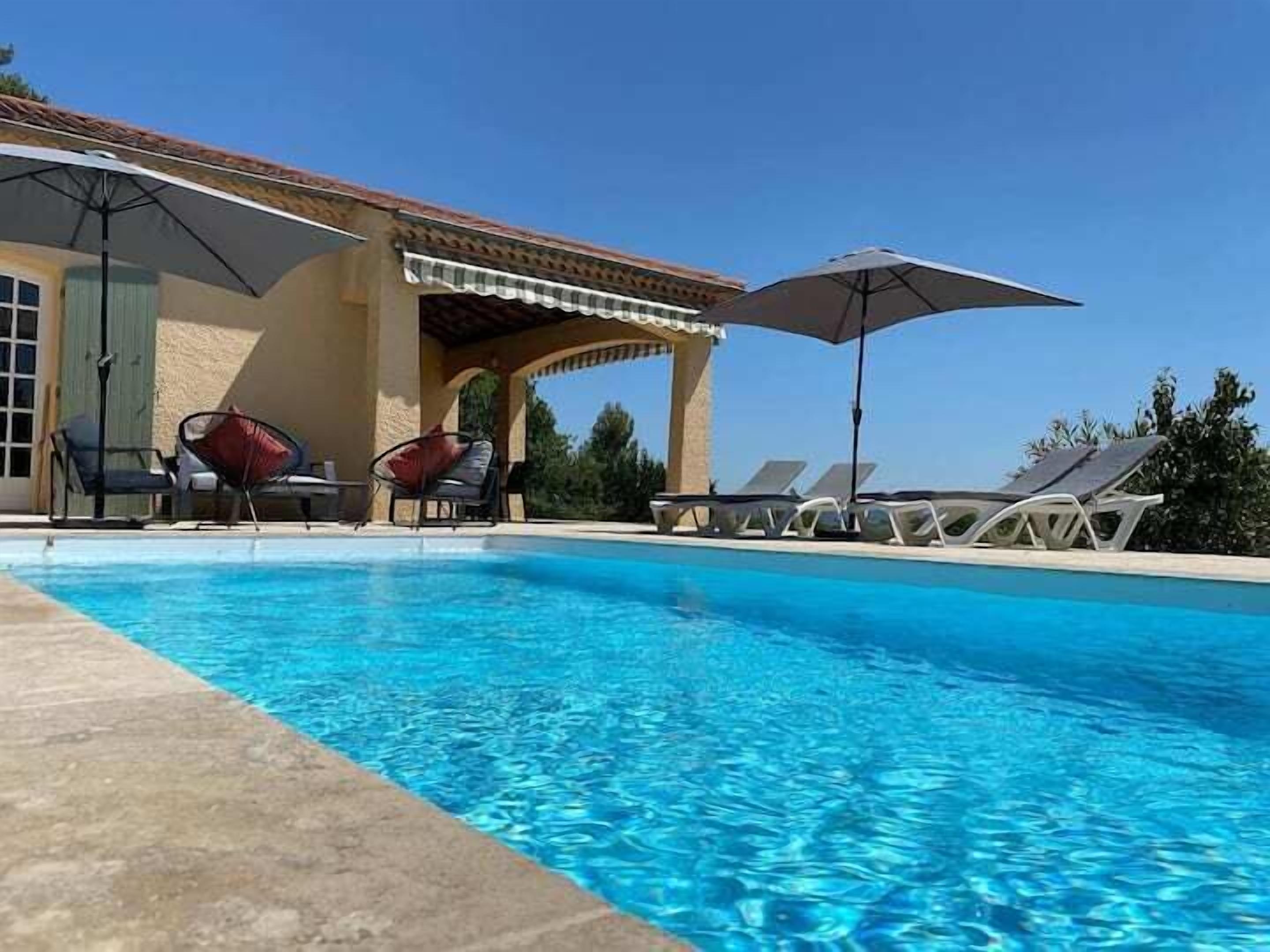 A swimming pool with lounge chairs and umbrellas, surrounded by a building with a tiled roof.