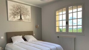 A bedroom with a large bed, a window with a view, a radiator, and a painting on the wall. - L'oustal de cigales, panoramic view (Lédignan)