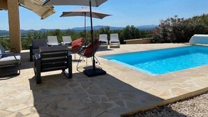 A poolside area with lounge chairs and umbrellas, a stone floor, and a view of the landscape. - L'oustal de cigales, panoramic view (Lédignan)