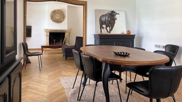 A dining area with a wooden table and black chairs, a fireplace, and a bull painting on the wall. - L'oustal de cigales, panoramic view (Lédignan)