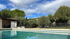 Piscina transparente con un borde de baldosas, rodeada de árboles y una zona vallada.