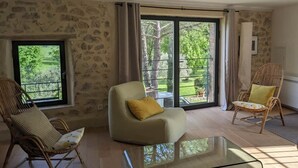 Un amplio salón con una mesa de centro de vidrio, dos sillones de mimbre y vistas a un jardín a través de grandes puertas corredizas de cristal.