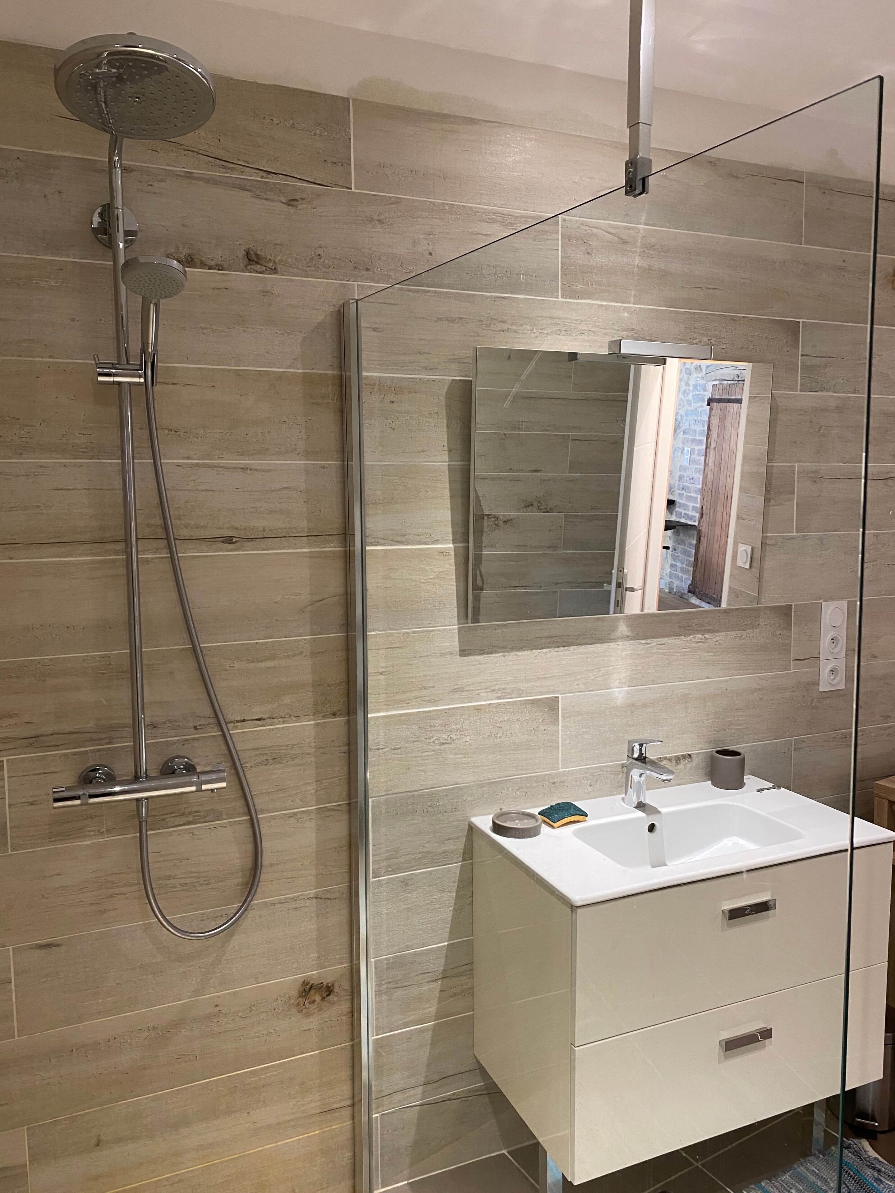 Un baño moderno con cabina de ducha de vidrio, tocador blanco con espejo y piso de baldosas.