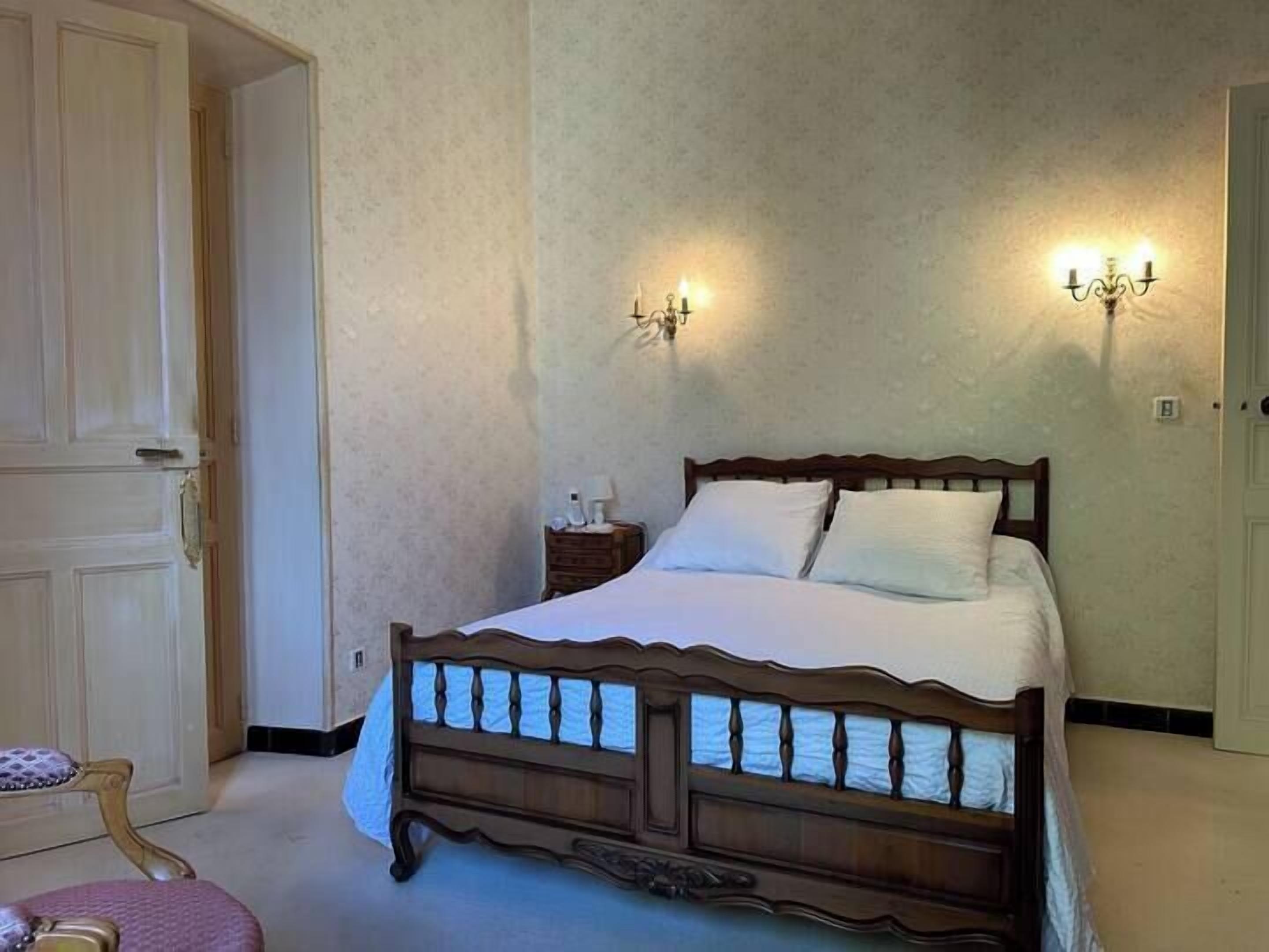 A bedroom with a wooden bed, two wall sconces, a nightstand, and a door.
