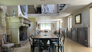 A spacious dining area with a long wooden table and chairs, a fireplace, and a chandelier. - Le mas d'Elise, in the heart of the Cévennes countryside (Saint-Hippolyte-de-Caton)