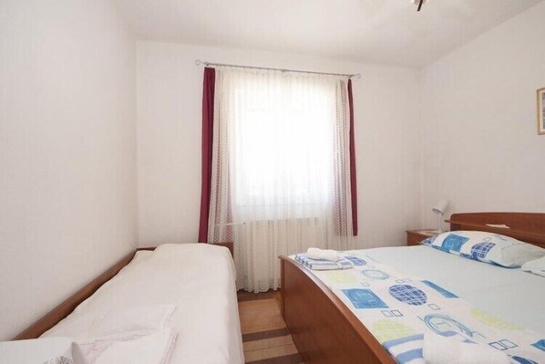 A hotel room with two single beds, a wooden headboard, a window with sheer curtains, and a bedside table with a lamp. - Two Bedroom Apartment with Terrace(A1) (Splitska)