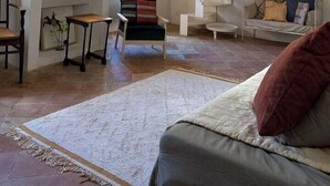 A spacious living room with a high ceiling, exposed beams, a staircase, and a cozy seating area. - Village house with swimming pool (Saint-Étienne-de-l'Olm)