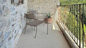 A stone balcony with a rustic wooden ceiling, a metal chair, a small table, and a potted plant. - Village house with swimming pool (Saint-Étienne-de-l'Olm)
