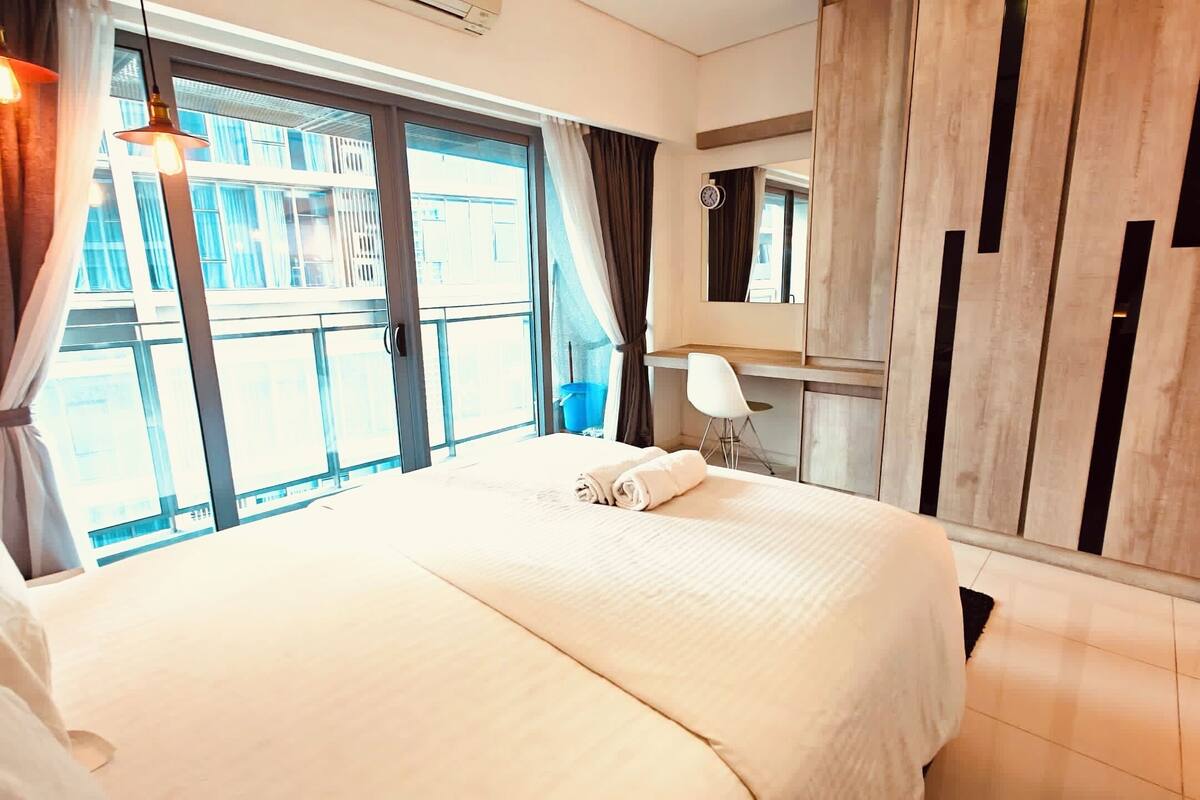 A hotel room with a large bed, a desk, a chair, and a window with curtains.