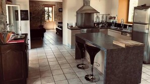 A modern kitchen with a large island, stainless steel appliances, and a stone wall in the background. - Le mas du figuier at the foot of the medieval city (Vézénobres)