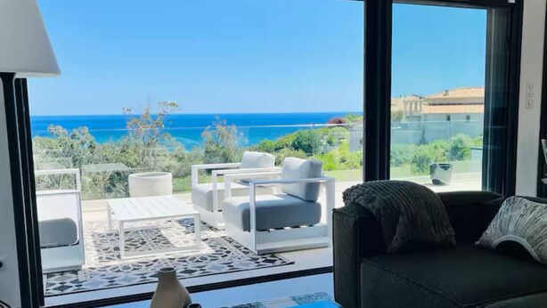 Una sala de estar moderna con un amplio ventanal que da a un balcón con vistas al océano.