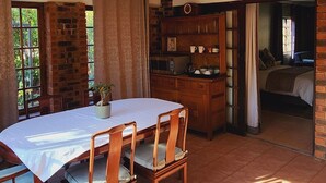 A dining area with a table and chairs, a brick wall, and a view of a bedroom through an open doorway. - Charming villa with WiFi in Gillitts (Gillitts)