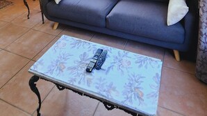 A living room with a sofa, a table with remote controls, a wooden cabinet, and a window with curtains. - Charming villa with WiFi in Gillitts (Gillitts)
