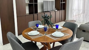 Uma área de refeições com uma mesa redonda, cadeiras estofadas cinzas e uma planta no centro.