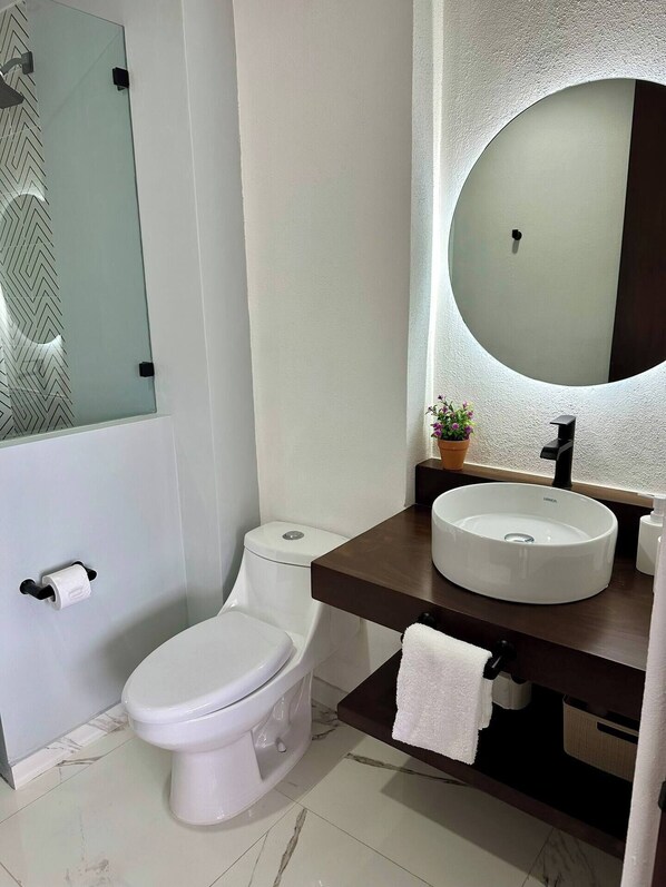 A modern bathroom with a toilet, a sink, a mirror, and a shower area.