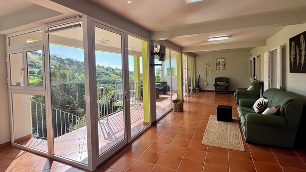 A spacious living area with a balcony, a green sofa, and a tiled floor. - Green House | Mountain Green Views & Sea Glimpse | Calheta (Calheta)
