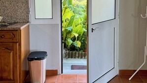 A room with a kitchen area, a trash bin, and a door leading to a garden. - Green House | Mountain Green Views & Sea Glimpse | Calheta (Calheta)