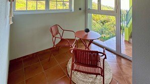 A room with a tiled floor, a round table with two chairs, and a view of greenery through large windows. - Green House | Mountain Green Views & Sea Glimpse | Calheta (Calheta)