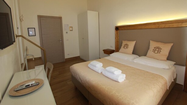 A hotel room with a bed, bedside tables, a desk with a remote control, and a chair. - Art Atelier Accomodation Camera 1 (ROMA)