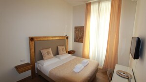 A neatly made bed with a wooden headboard, a bedside table, and a wall-mounted TV. - Art Atelier Accomodation Camera 1 (ROMA)