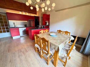 A compact kitchen with red cabinets, a dining table with floral tablecloths, and a chandelier.