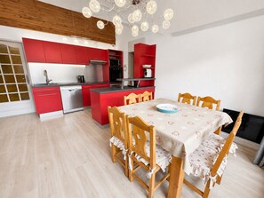 Une cuisine moderne avec des meubles de rangement rouges, une table à manger recouverte d’une nappe à motifs floraux et des chaises en bois.