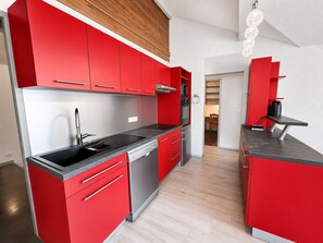 Une cuisine moderne avec des meubles de rangement rouges, des appareils électroménagers en acier inoxydable et un plafond en bois.
