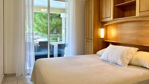 Una camera d'albergo con un letto, una testiera in legno, un balcone con mobili da esterno e vista sul verde.