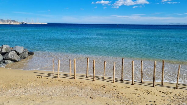 Una spiaggia con acque cristalline, una riva sabbiosa e un recinto in legno.