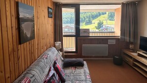 A wooden-paneled room with a sofa, a television, and a view of a green landscape through a window. - Apartment on the slopes in Super Besse (Besse-et-Saint-Anastaise-Super Besse)