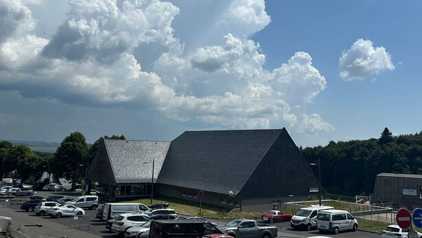 A building with a sloped roof, surrounded by parked cars and a clear sky with clouds. - Apartment on the slopes in Super Besse (Besse-et-Saint-Anastaise-Super Besse)