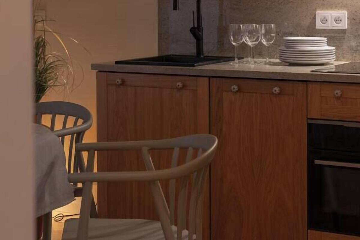 A compact kitchen with wooden cabinets, a countertop, a sink, and a chair.