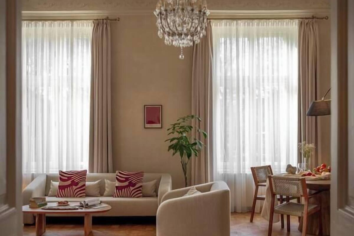 Un salon spacieux agrémenté d’un lustre, d’un canapé, d’une table basse et d’un coin repas avec des chaises et une table.