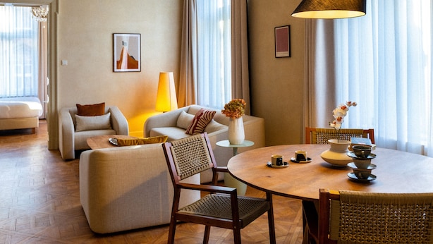 Amplia sala de estar con sofá, sillones, una mesa redonda de madera y una mesa de comedor preparada para dos.
